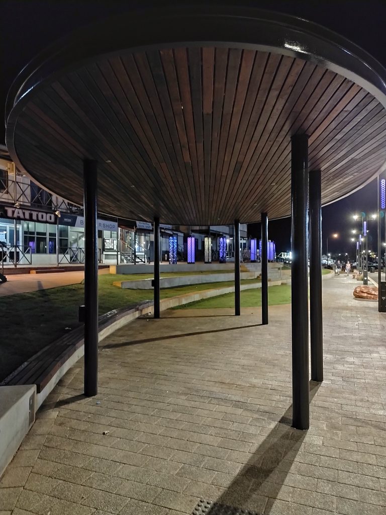 Underside view of oval shaded steel framed structure in Broome's Chinatown showing timber panelling and usb charger ports.